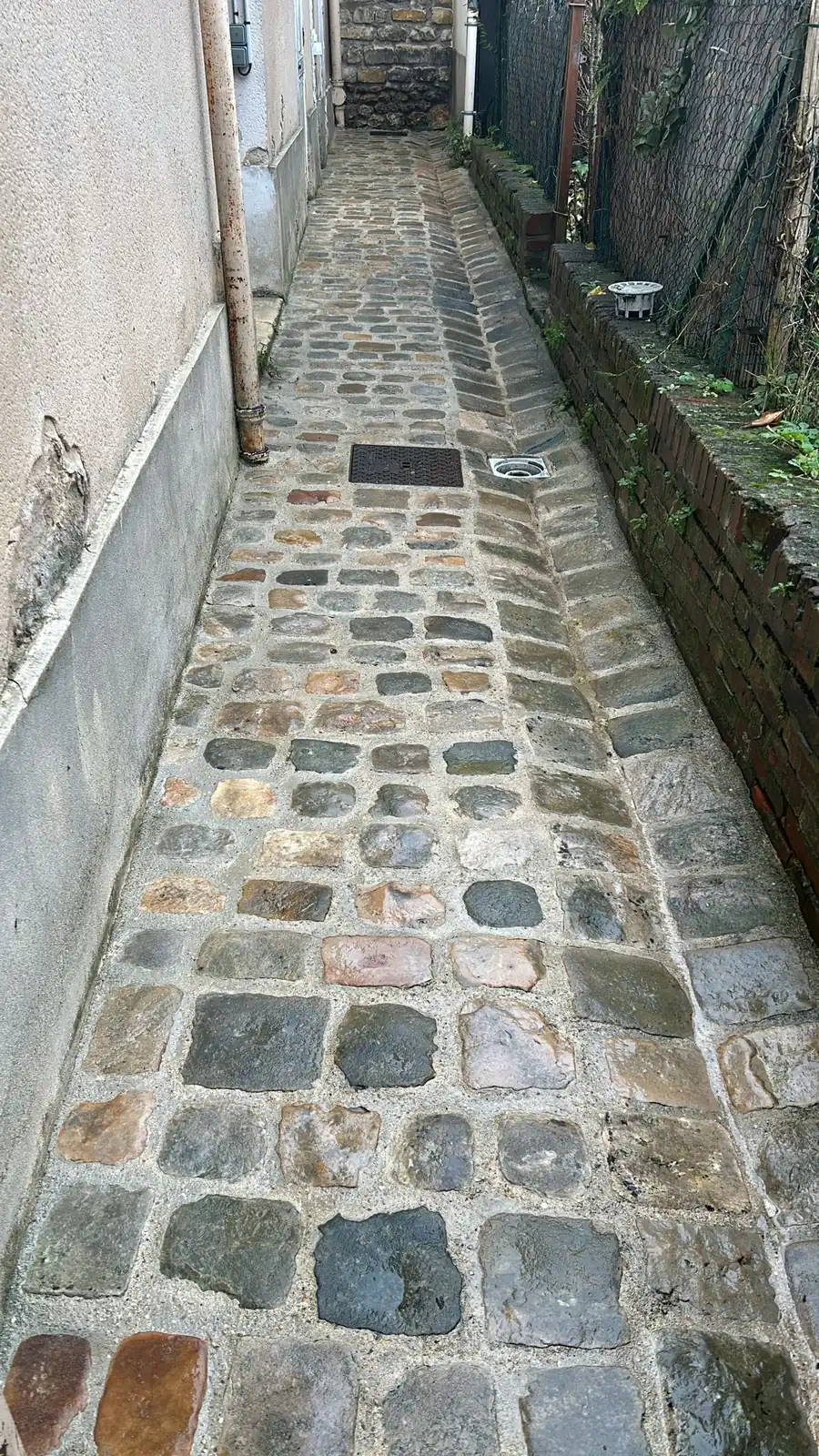 Passage étroit en pavés de granit lavés, le long d’un mur de maison