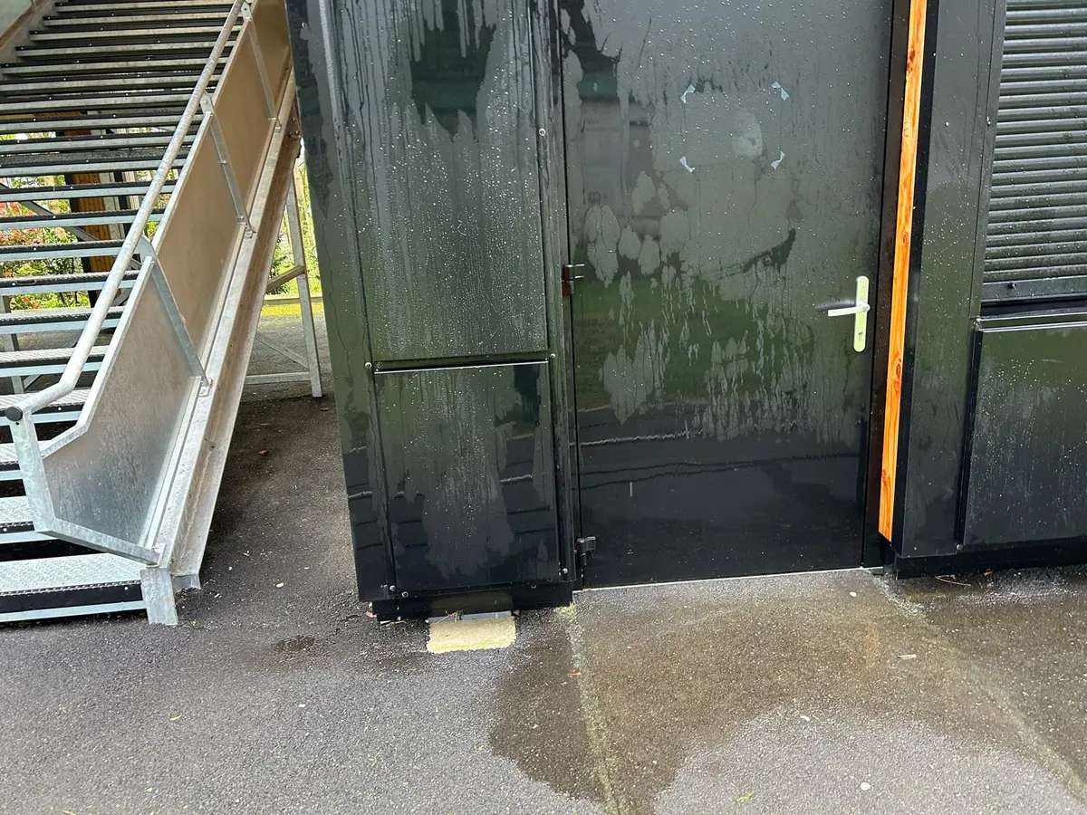 Porte et panneaux de bardage noir en cours de lavage : les traces claires du produit et de l’eau, le pied d’un escalier métallique à gauche