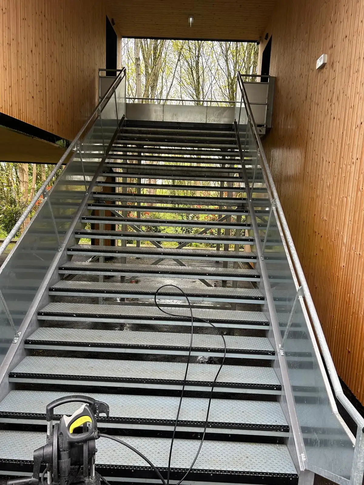Le même type d’escalier métallique après le lavage, marches nettes et brillantes, le nettoyeur haute pression posé en bas