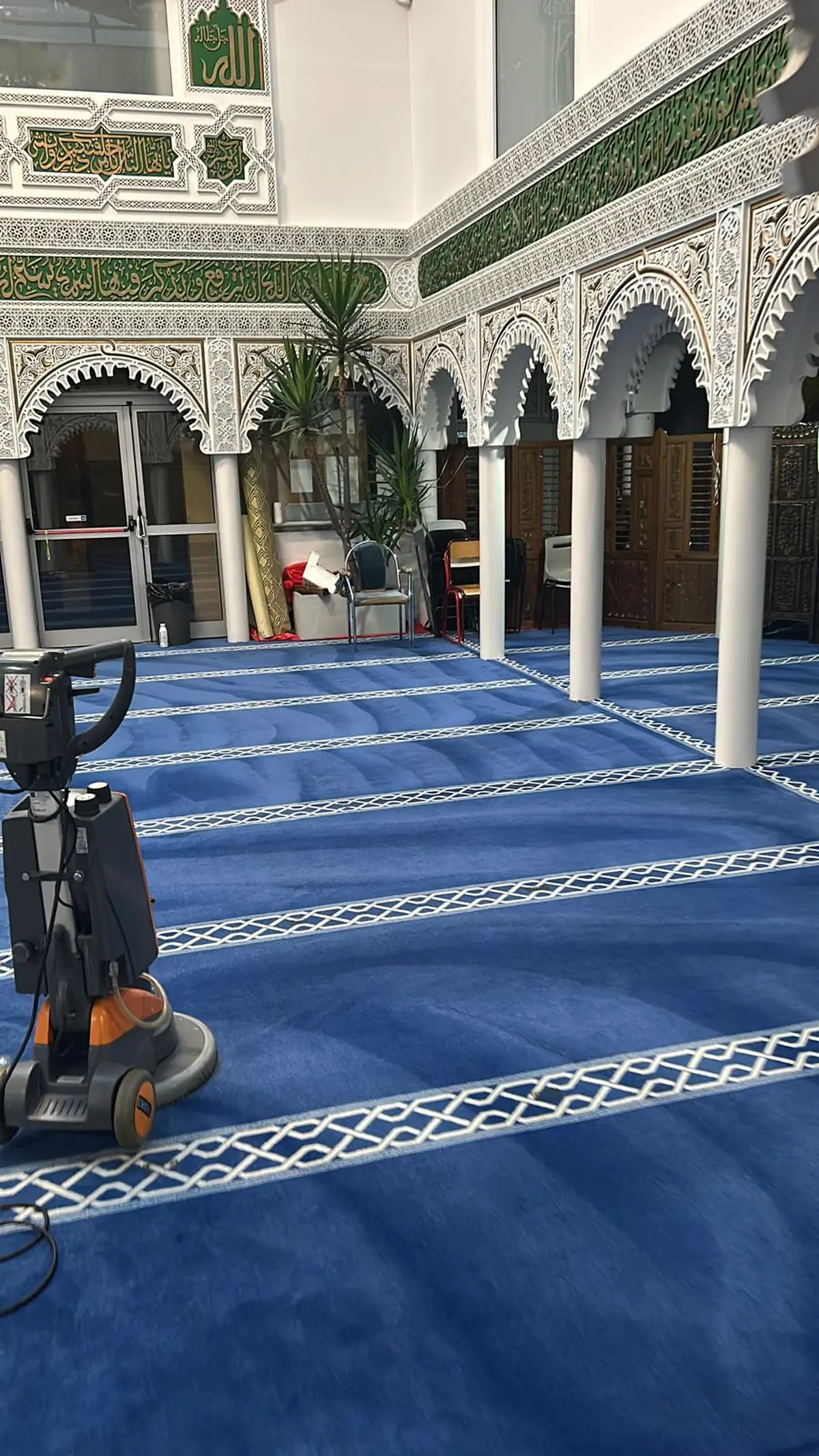 Grande salle à moquette bleue à motifs, colonnes et arcades au fond, la machine d’injection-extraction au premier plan